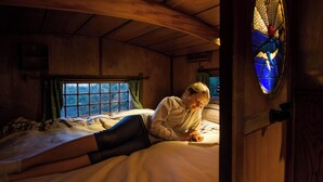 Ein gemütliches Zimmer mit einem Bett, einem Fenster mit Vorhängen und einer Holztür mit einem Buntglasfenster.