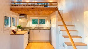 A modern kitchen with wooden beams, a mezzanine level, and a staircase. - Tiny Greenie - Passive Tiny House, Golden Bay (Takaka)