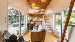 A cozy interior with a wicker sofa, wooden flooring, and a staircase leading to an upper level. - Tiny Greenie - Passive Tiny House, Golden Bay (Takaka)