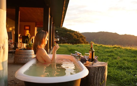 A person relaxing in a hot tub with a scenic view of hills and a sunset.