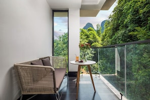 A balcony with a wicker chair and a small table with a drink and flowers. - Yangshuo 1Q84 Tree Hotel (Guilin)