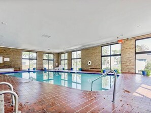 An indoor swimming pool with clear glass walls, a tiled floor, and a lifebuoy on the wall.