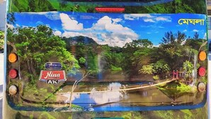 Vista trasera de un autobús con un mural de un paisaje pintoresco, el logotipo de Hino A.K. y una placa de matrícula verde.
