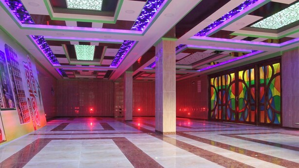 Un vestíbulo amplio con piso de baldosas, techo alto con iluminación decorativa y un ventanal de vitral colorido.