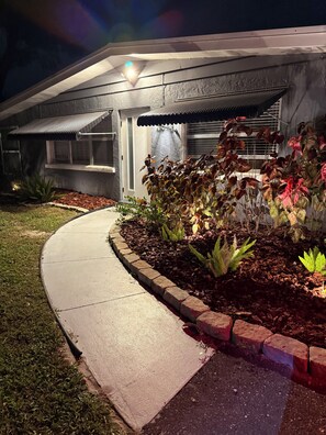 A modern house with a covered porch, a well-maintained garden with various plants, and a paved driveway. - White Bird of Paradise Heated Pool Fire Pit Near Siesta Key outdoor bar (Sarasota)