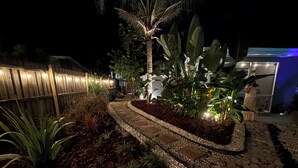 Ein Garten bei Nacht mit einem Kiesweg, Palmen und einem Holzzaun.