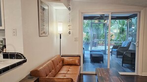 Ein modernes Wohnzimmer mit einer Ledersofa, einem Holztisch und einem Esstisch. Ein Schiebeglasfenster führt zu einer Außenpatio-Terrasse mit Möbeln.