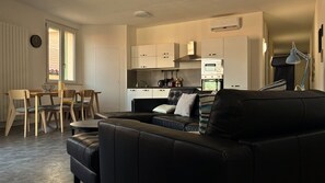 Ein modernes Wohnzimmer mit einer schwarzen Ledersofa, einem Essbereich mit Holzsesseln, einer Küche mit weißen Schränken und einem Fenster mit Blick.