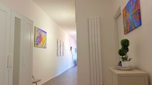 Un couloir aux murs blancs, avec un tapis beige et une plante en pot posée sur un meuble.