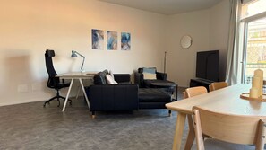 Ein modernes Wohnzimmer mit Schreibtisch, einer Couch, einem Fernseher und Kunstwerken an der Wand.