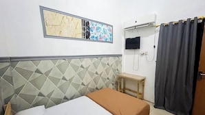A room with a bed, a small table, a TV mounted on the wall, and a curtain. - Rumi Hotel (Malang)