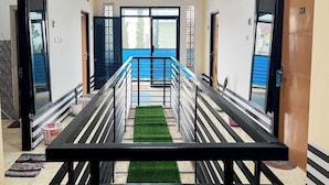 A hallway with a central bench, doors on either side, and a view of a blue outdoor area. - Rumi Hotel (Malang)