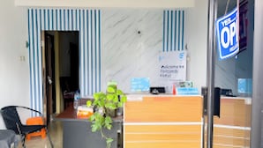A reception area with a wooden desk, a potted plant, and a sign with text. - Rumi Hotel (Malang)