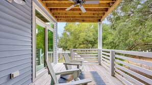 Varanda coberta com duas cadeiras Adirondack, um ventilador de teto e vista para árvores e um deck.