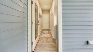 Um corredor estreito com piso de madeira, um tapete de entrada e uma porta no final.