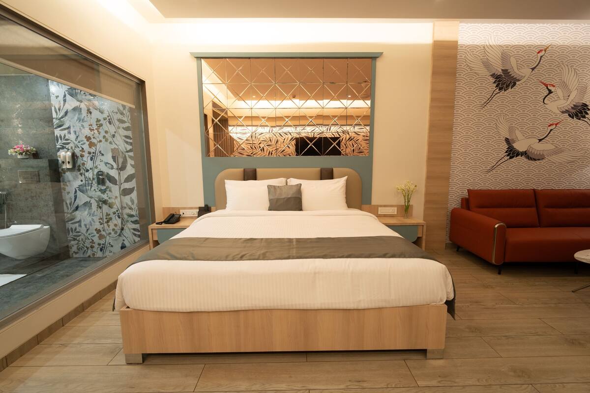 Un dormitorio moderno con una cama grande, una cabina de ducha de vidrio, un cabecero de madera y un sofá rojo.
