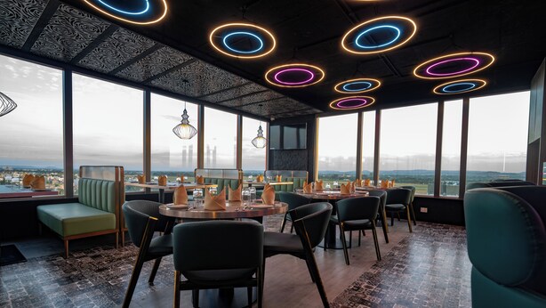 A modern dining area with round tables, chairs, and a view of the cityscape through large windows. - Pride Elite Chhatrapati Sambhaji Nagar (Chhatrapati Sambhajinagar)