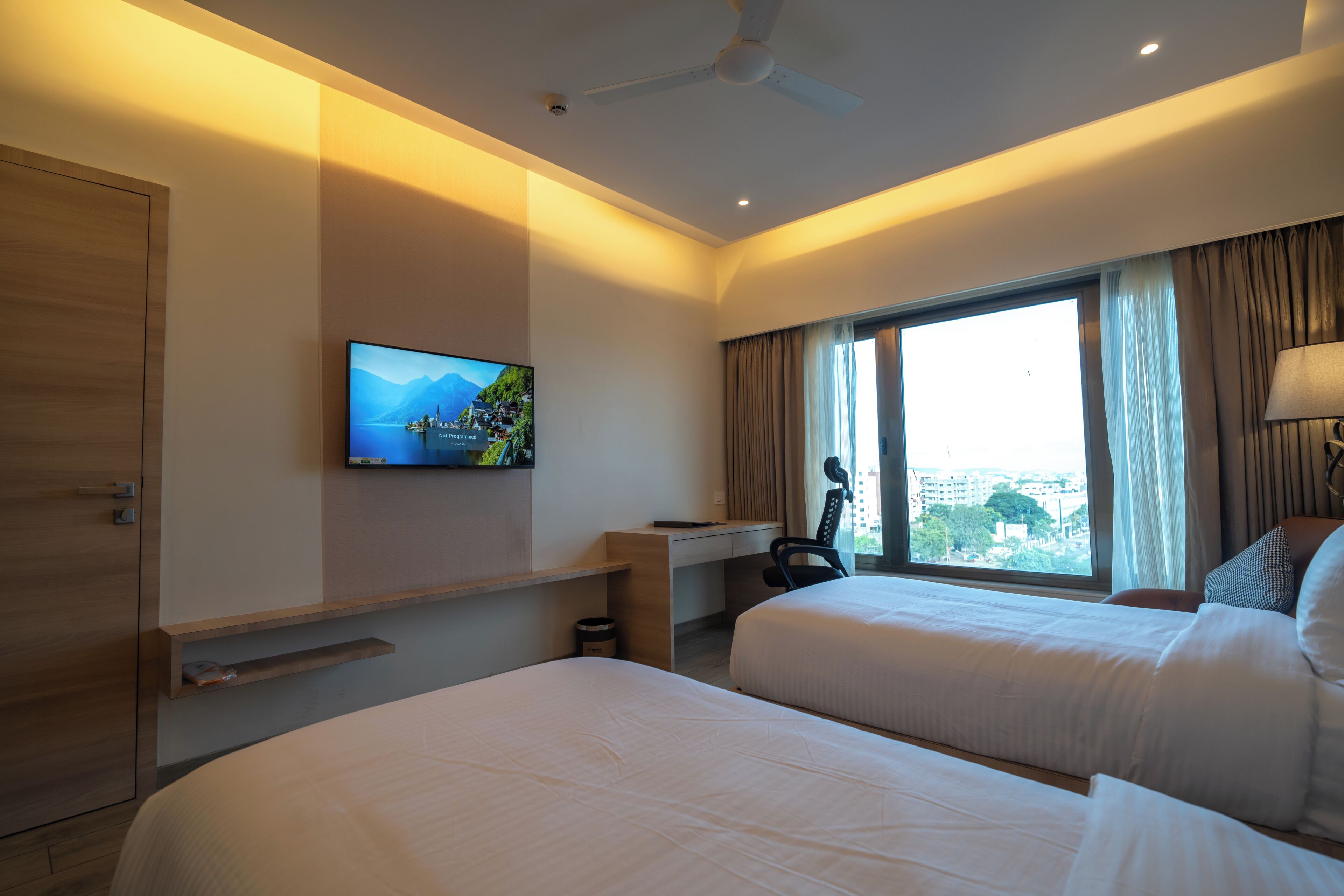 A hotel room with two beds, a desk, a television, and a window with curtains.