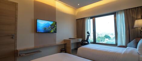 A hotel room with two beds, a desk, a television, and a window with curtains.