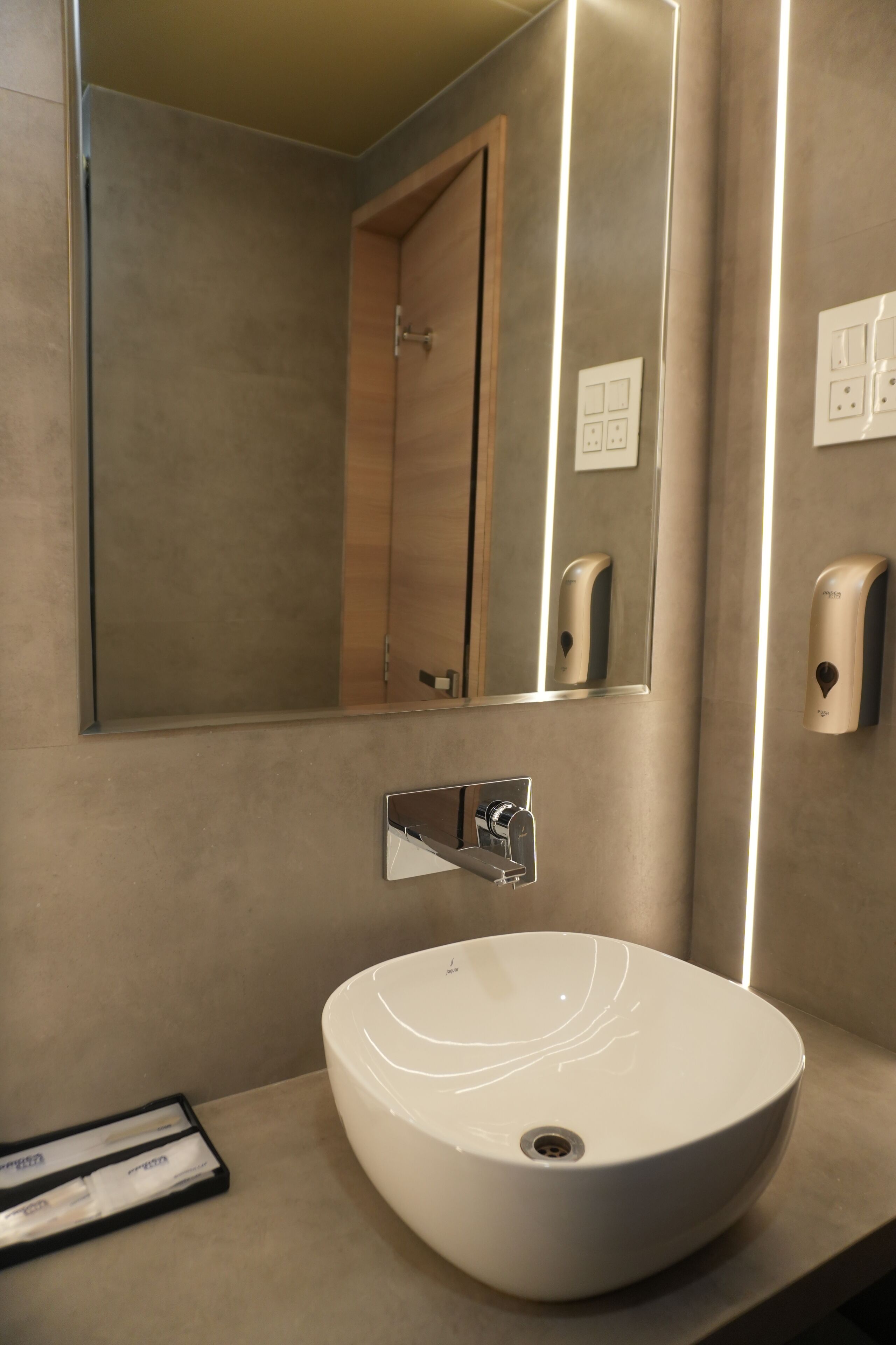 Une salle de bain moderne avec un grand miroir, un lavabo blanc et un distributeur de savon.