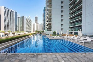 A modern swimming pool with lounge chairs and a cityscape in the background. - Stayshort - 1 Bed in Business Bay Sleeps 2 With City View (Dubai)