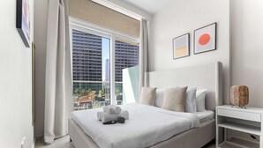 A modern hotel room with a large bed, a bedside table, and a view of a cityscape through a large window. - Stayshort - 1 Bed in Business Bay Sleeps 2 With City View (Dubai)