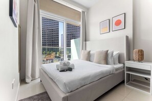 A modern hotel room with a large bed, a bedside table, and a view of a cityscape through a large window. - Stayshort - 1 Bed in Business Bay Sleeps 2 With City View (Dubai)