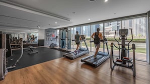 A modern gym with treadmills, weight machines, and a large window offering a city view. - Stayshort - 1 Bed in Business Bay Sleeps 2 With City View (Dubai)