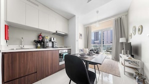 A modern kitchen with white cabinets, a wooden countertop, and a dining area with a black chair and table. - Stayshort - 1 Bed in Business Bay Sleeps 2 With City View (Dubai)
