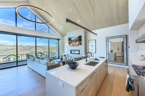 A modern kitchen with a large island, a dining area with a view, and a living space with a balcony overlooking a mountainous landscape. - Labor Day Sale - Limited Time Offer, Save up to 30% (Francis)