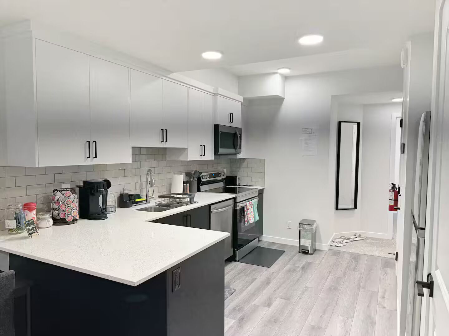 A modern kitchen with white cabinets, a black microwave, and a stainless steel sink.