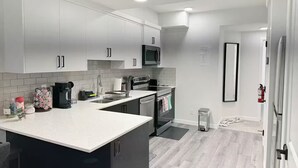 A modern kitchen with white cabinets, a black microwave, and a stainless steel sink. - Clean, Cozy, Comfy & Modern (Calgary)