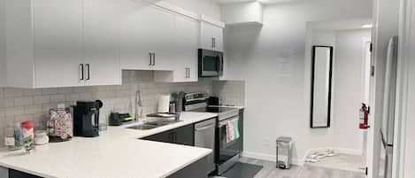 Une cuisine moderne avec des meubles blancs, un micro-ondes noir et un évier en acier inoxydable.