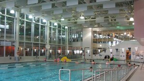 An indoor swimming pool with clear lanes, a safety railing, and a high ceiling with industrial lighting. - Clean, Cozy, Comfy & Modern (Calgary)