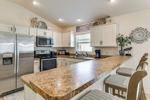 A kitchen with white cabinets, stainless steel appliances, a granite countertop, and a bar stool seating area. - Loving Sunny Days in The Villages (Wildwood)