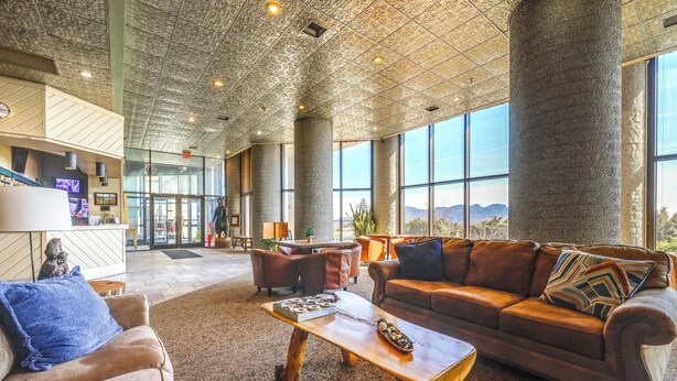 Eine geräumige Lobby mit hoher Decke, großen Fenstern und einer zentralen Sitzecke mit Sofa und Couchtisch.