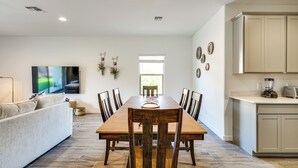 Uma sala de jantar com uma mesa e cadeiras de madeira, um sofá e uma cozinha com armários e eletrodomésticos.
