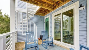 Un porche cubierto con sillas azules, una terraza de madera y una escalera de caracol.