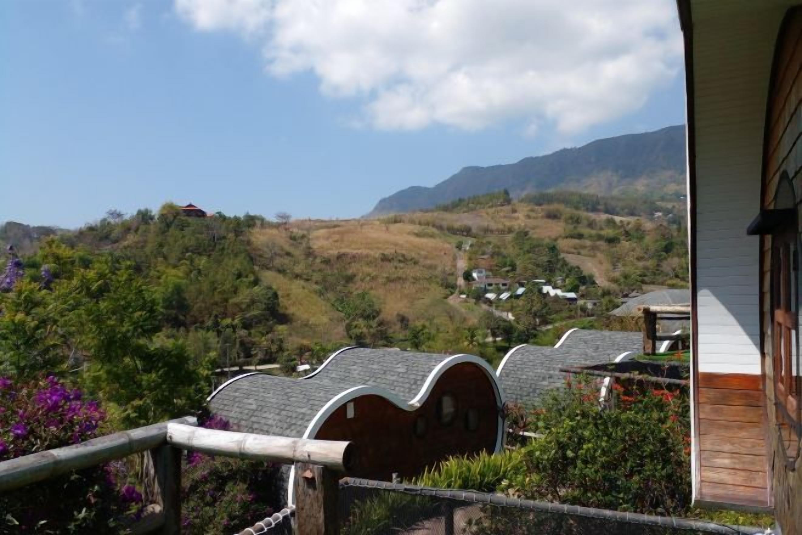 A view from a building with a wooden balcony overlooking a valley with houses and mountains.