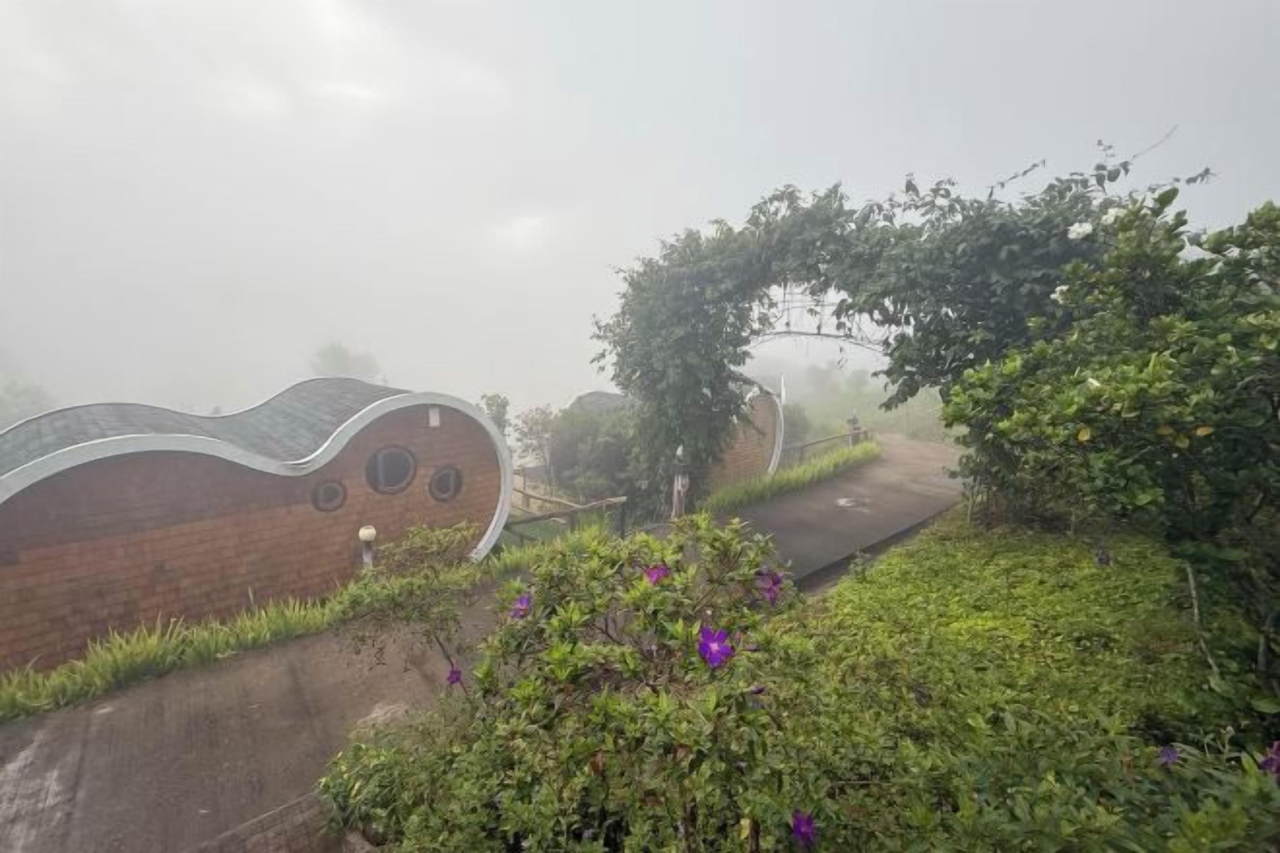 A brick building with a curved roof and circular windows, surrounded by greenery and a pathway.