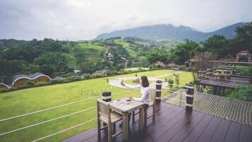 A wooden deck with a table and chairs overlooking a lush green landscape with hills and a clear sky.