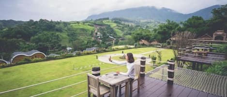 A wooden deck with a table and chairs overlooking a lush green landscape with hills and a clear sky.