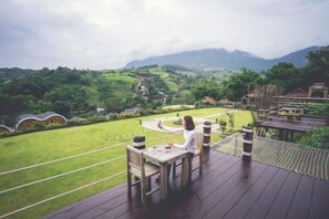 A wooden deck with a table and chairs overlooking a lush green landscape with hills and a clear sky. - Kiri Pura Resort Khao Kho (Khao Kho)