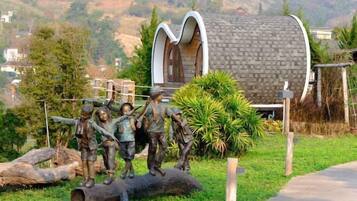 A unique cylindrical building with a sloped roof, surrounded by a grassy area with a sculpture of children and a large tree.