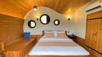 A bedroom with a wooden ceiling, a bed with pillows, a bench, and a wardrobe.