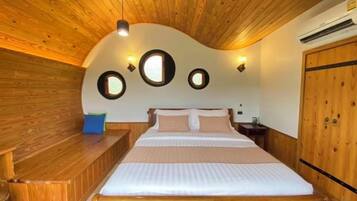 A room with a wooden ceiling, a bed with white bedding, a bench, and a wooden wardrobe.
