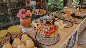 A buffet setup with various dishes and utensils, a vase with flowers, and a view of greenery through a window.