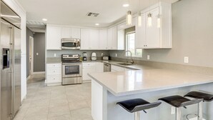 A modern kitchen with white cabinetry, stainless steel appliances, a large island with bar stools, and pendant lighting. - 7 Mi to Fremont St: Vegas Home w/ Backyard Oasis! (North Las Vegas)