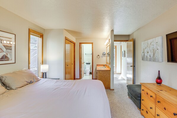 A bedroom with a bed, a dresser, a vanity, and a bathroom visible through an open door. - Private Hot Tub & SHARC Passes! Sunriver Home (Sunriver)