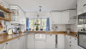 Une cuisine avec des meubles blancs, un plan de travail en bois, une fenêtre avec des rideaux bleus et divers appareils de cuisine.